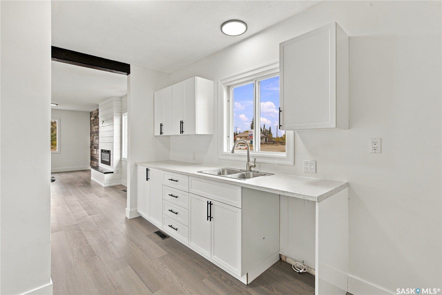 White cabinetry with matte black hardware, dual basin stainless steel sink, light-toned countertops, and wood-finish flooring