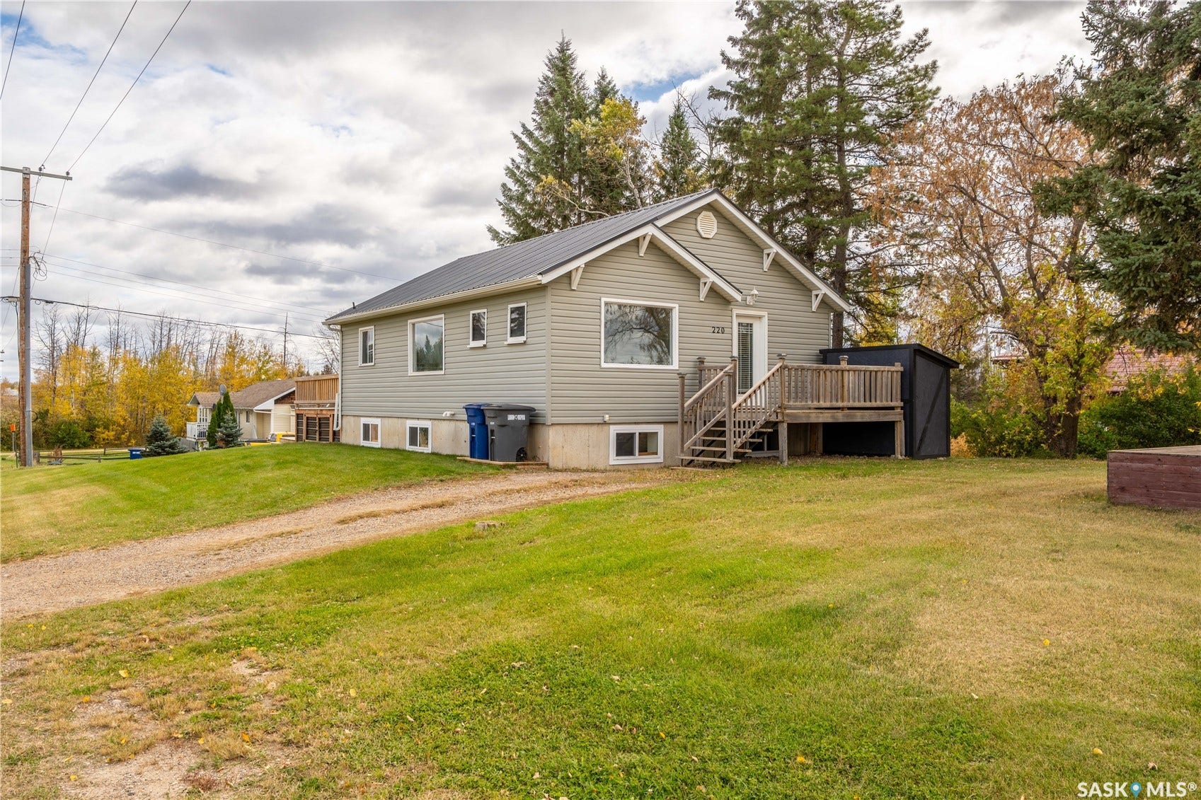 Siding exterior with a gable roof, elevated wooden deck, and a gravel driveway