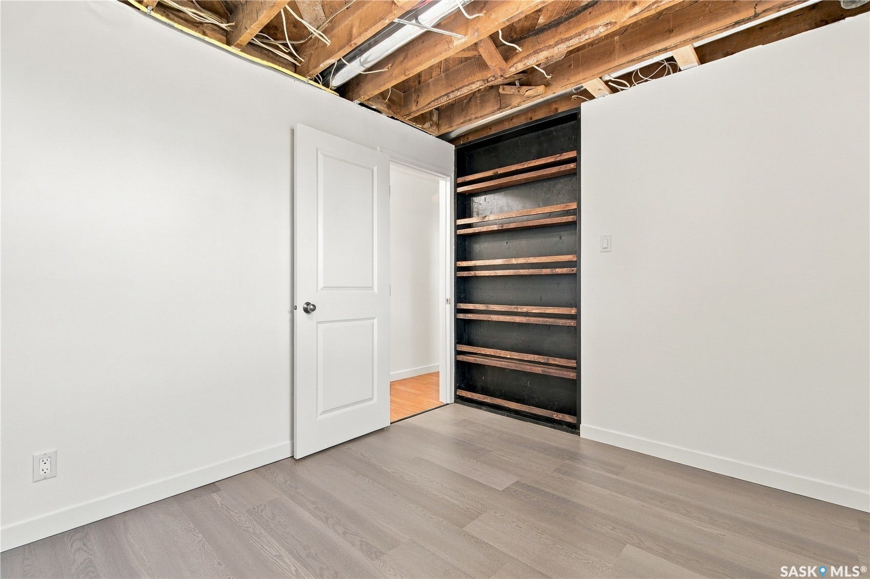 Light gray wood-finish flooring, white painted walls, white two-panel door, and built-in shelving