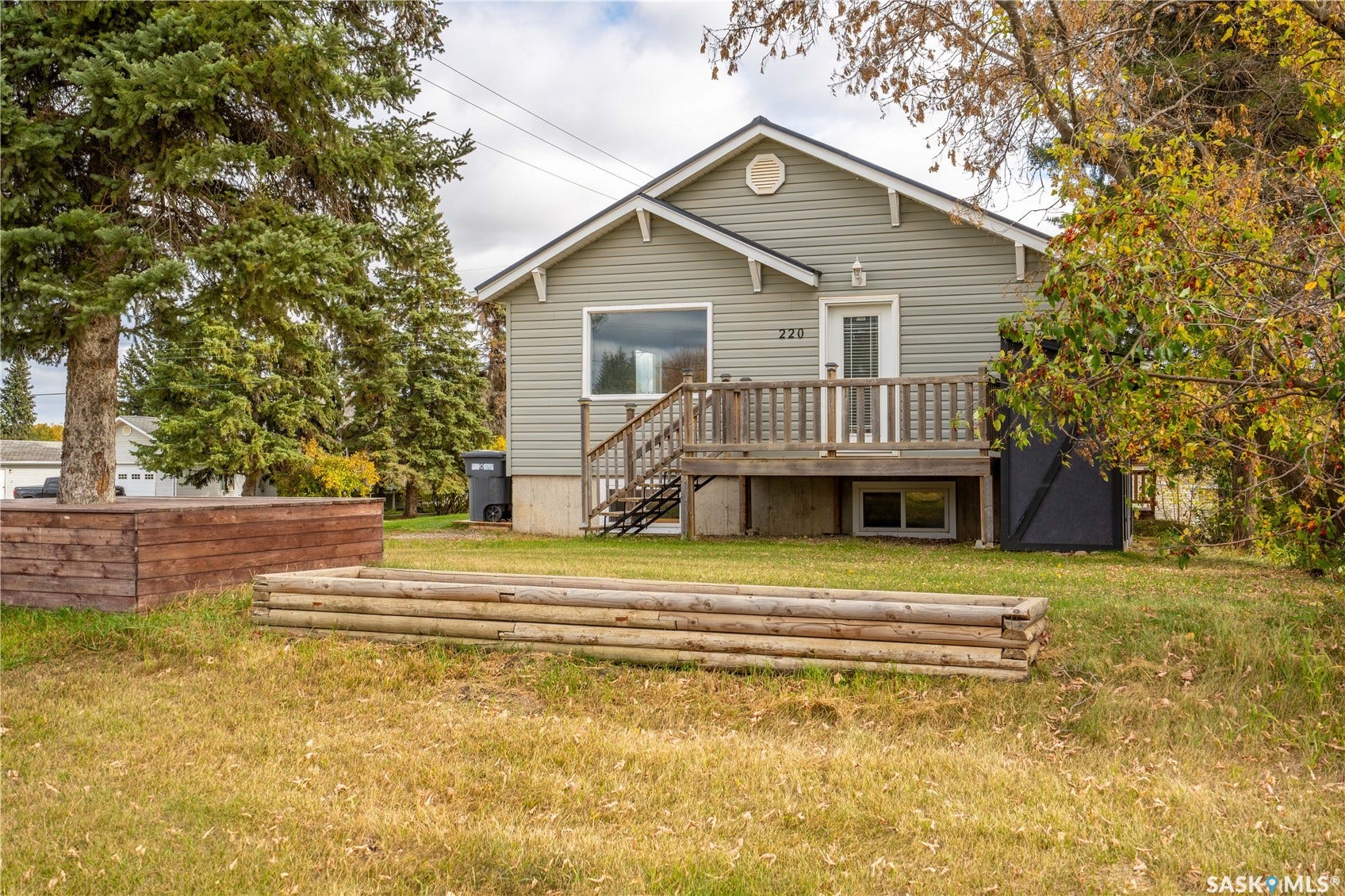 Siding exterior with a covered porch, wood deck with railings, and established perimeter trees