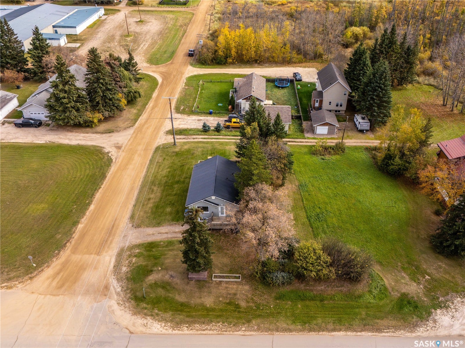 Expansive lot with mature trees and a detached garage, featuring a gravel road approach