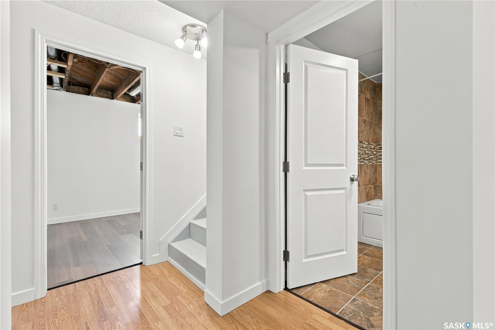 White interior walls, wood-finish flooring, white paneled interior doors, track lighting fixture