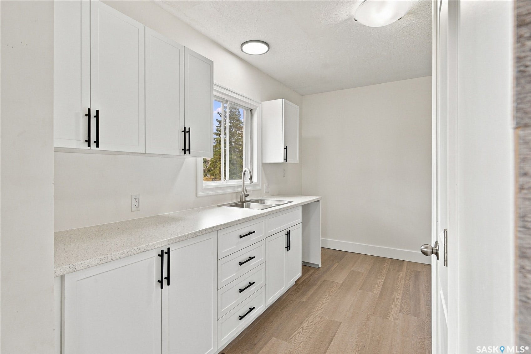 White cabinetry with matte black hardware, light-toned wood-finish flooring, white countertops, stainless steel sink, and recessed lighting