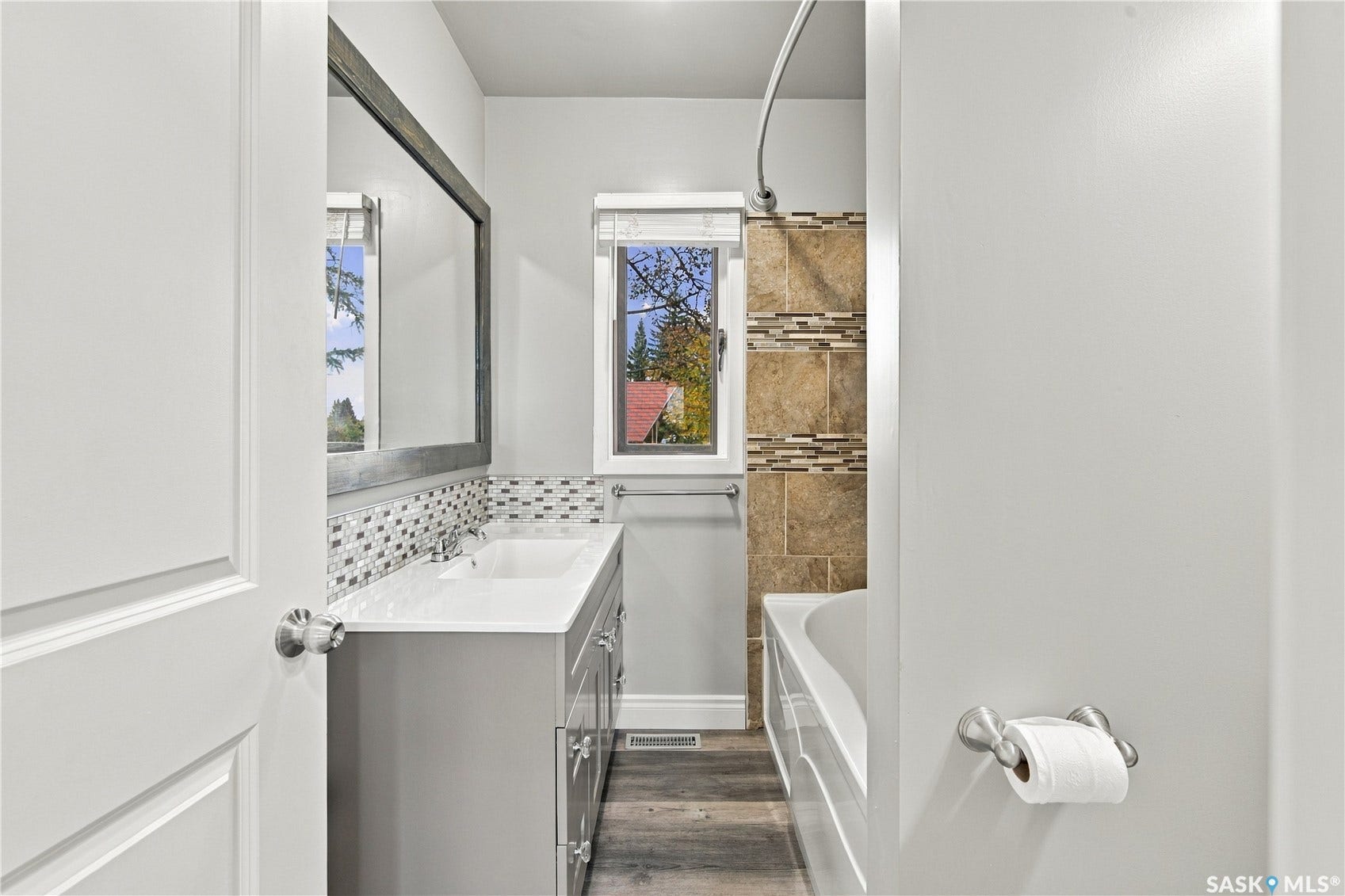 Bathroom with wood-finish flooring, a vanity with an integrated sink, a large framed mirror, and a tiled shower/tub combination