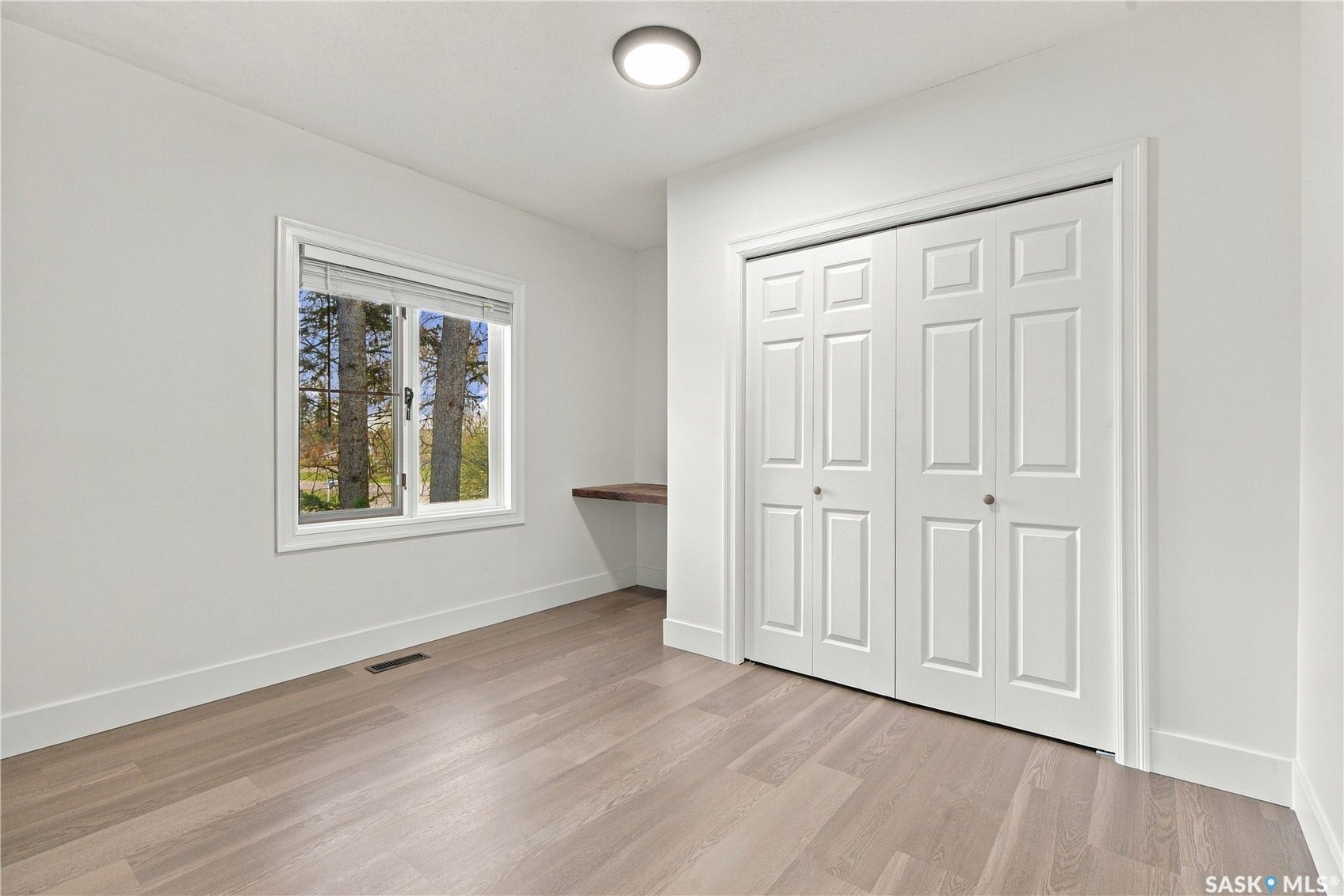 Light wood-finish flooring, white walls, built-in wooden desk, white paneled bifold closet doors, and recessed lighting