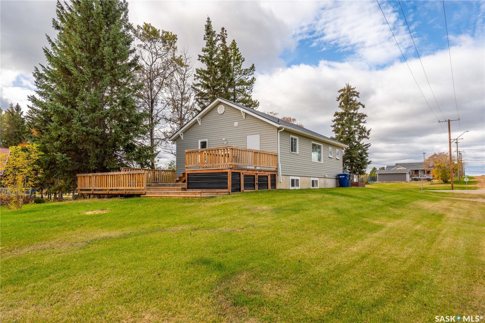 Expansive sloped lawn with mature trees and a multi-level wooden deck