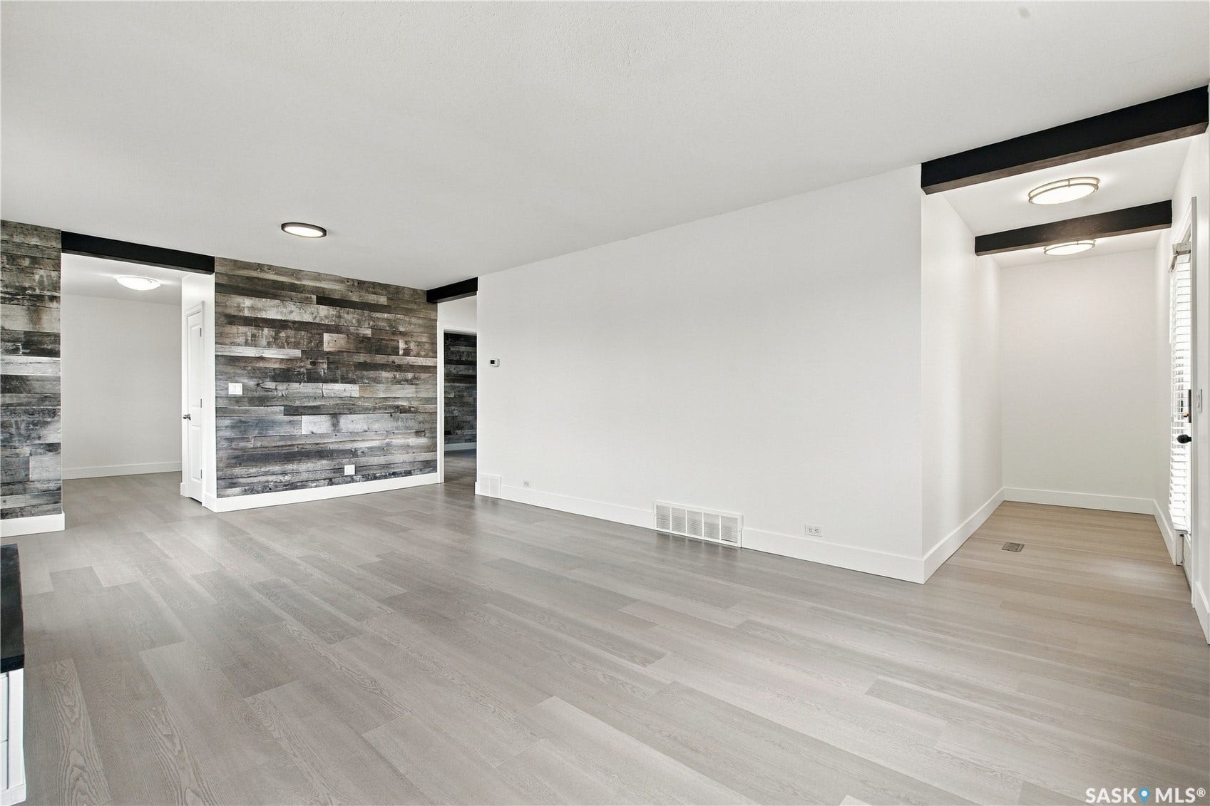 Light wood-finish flooring throughout, accent wall with wood paneling, white walls, and flush-mount ceiling lighting