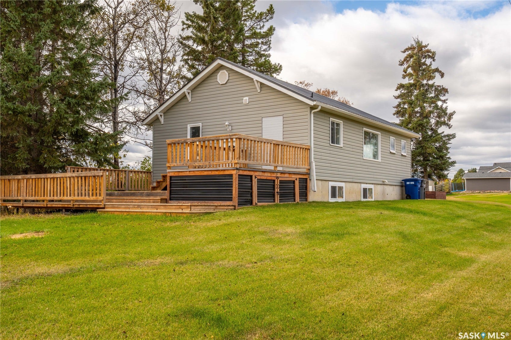 Expansive green lawn surrounds the residence, featuring a multi-level wooden deck with natural wood railings