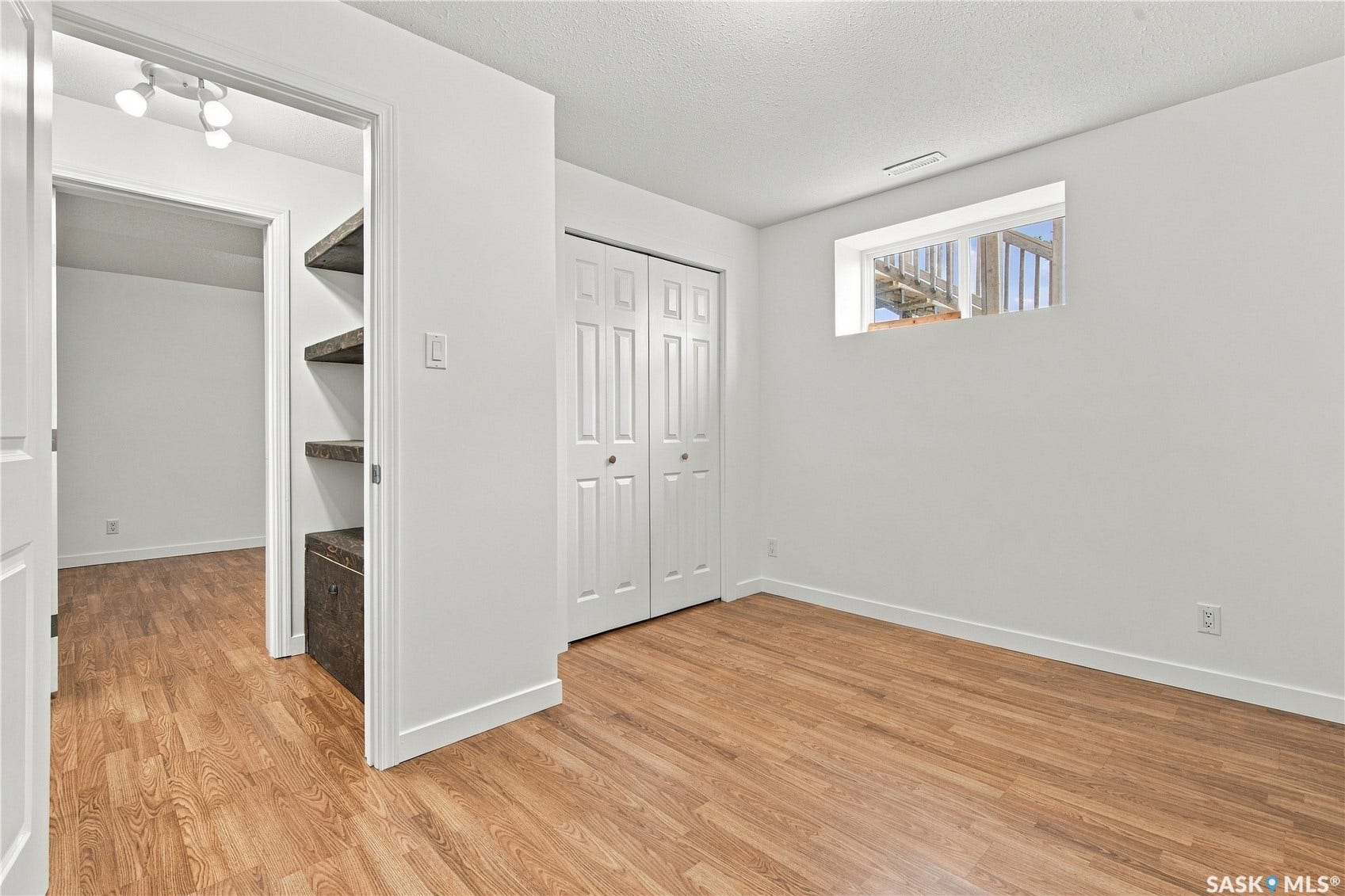 Wood-finish flooring, white bi-fold closet doors, built-in shelving, white trim, and a high window