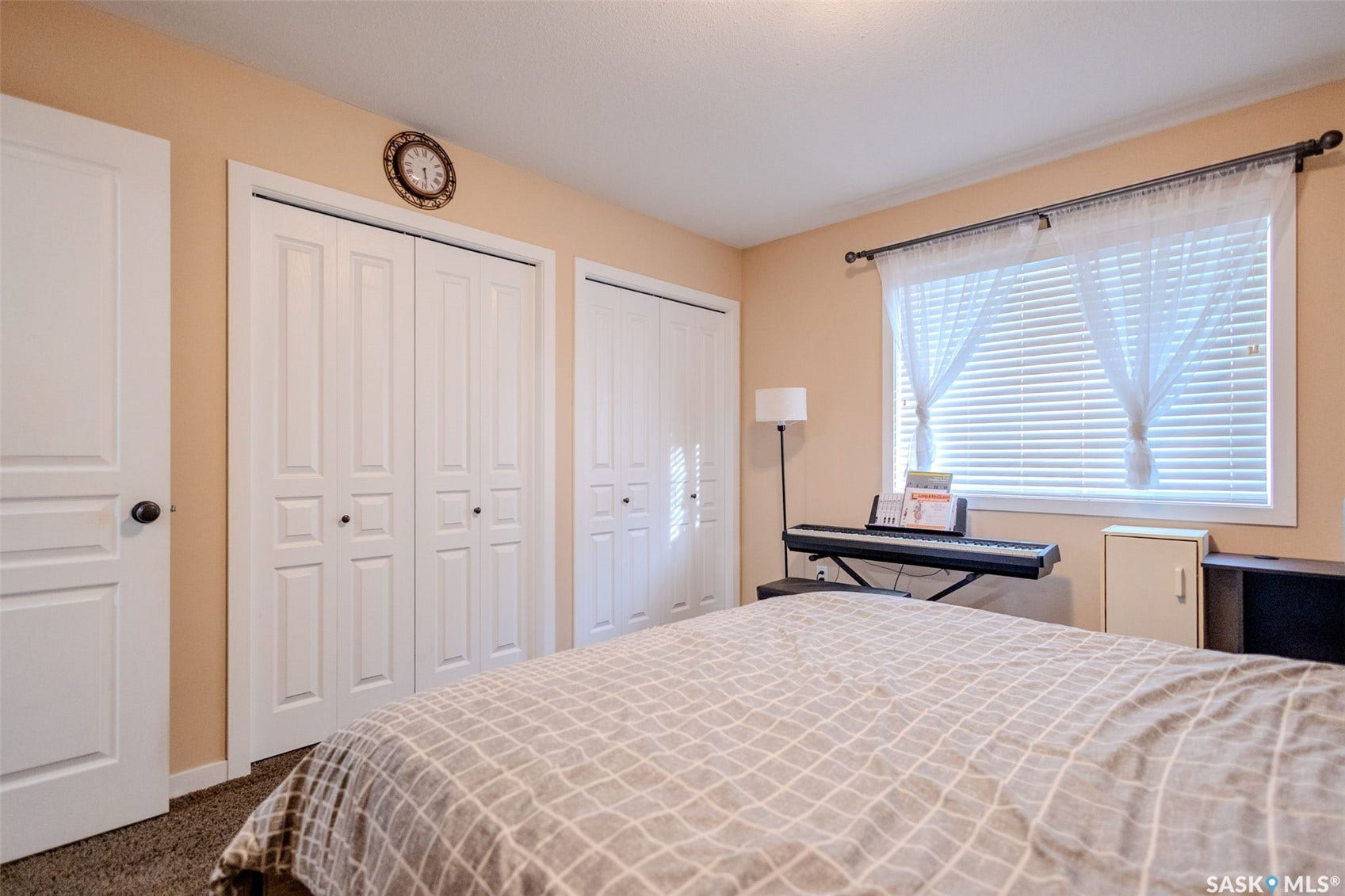Room featuring a window with blinds, two bi-fold closet doors, a panel door, and carpet flooring