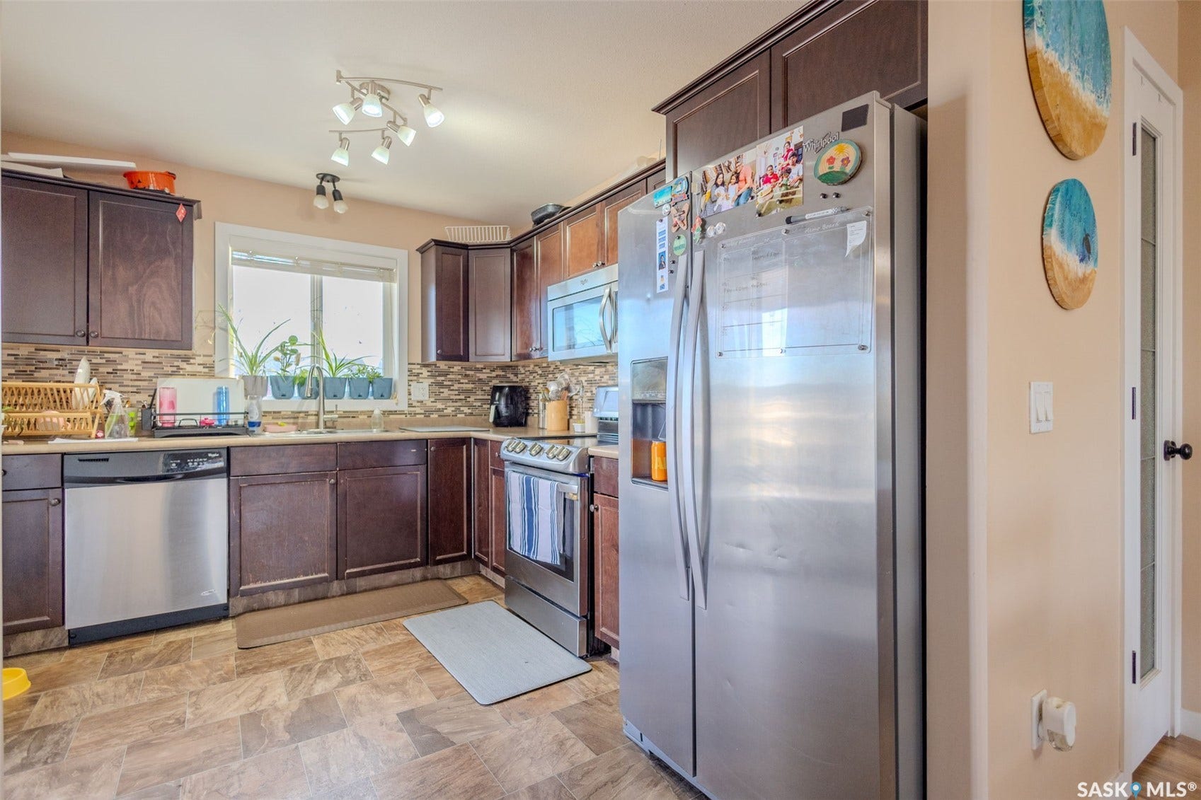 Kitchen featuring dark wood-finish cabinetry, stainless steel appliances, a tile backsplash, and a window above the sink
