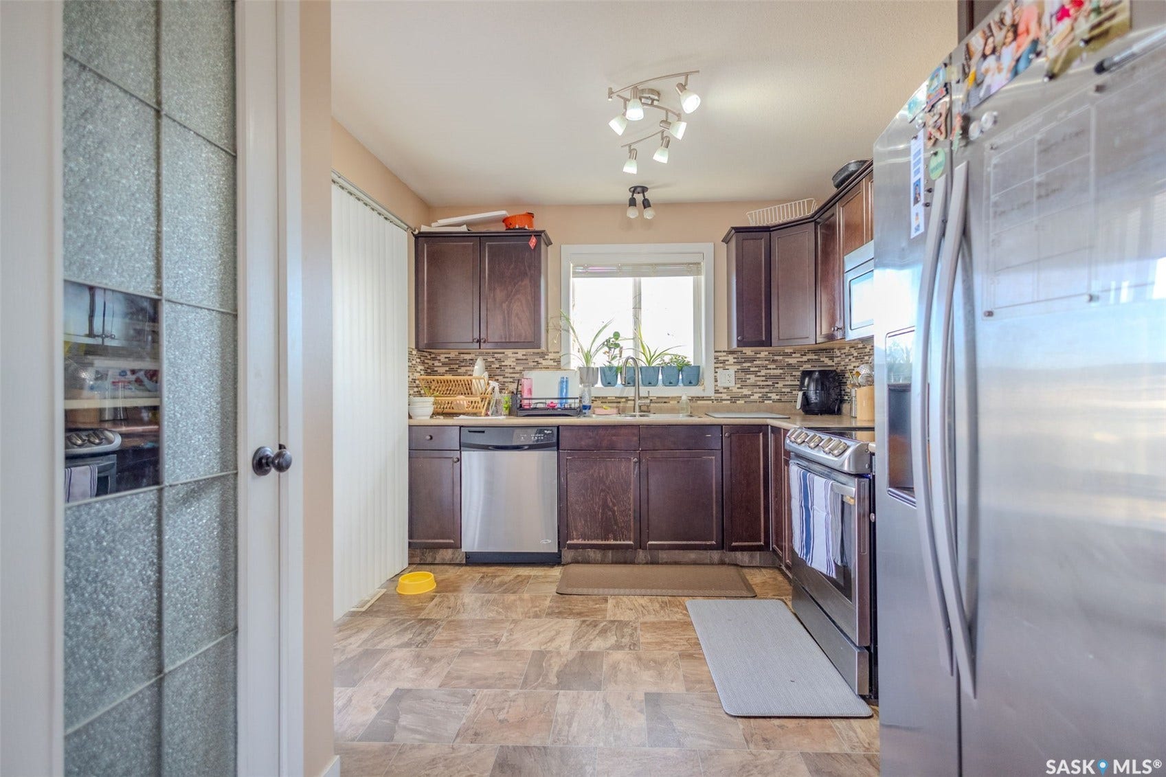 Kitchen with dark wood cabinetry, stainless steel appliances, mosaic tile backsplash, and track lighting