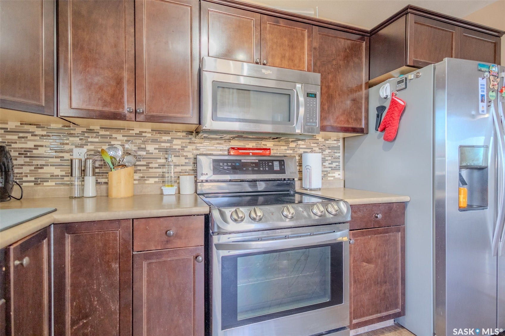 Stainless steel appliances, wood-finish cabinetry, tile backsplash, and light-toned countertops