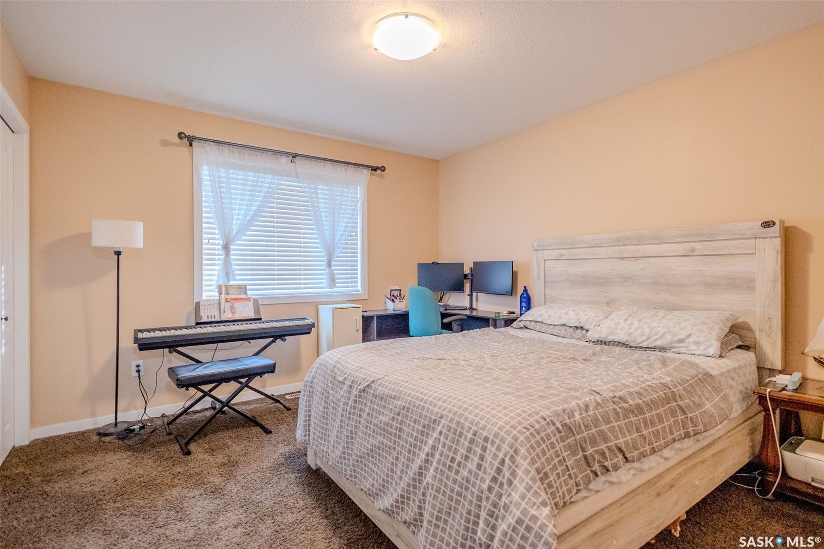 Spacious primary bedroom featuring a light wood-finish bed frame, carpet flooring, and warm neutral wall tones