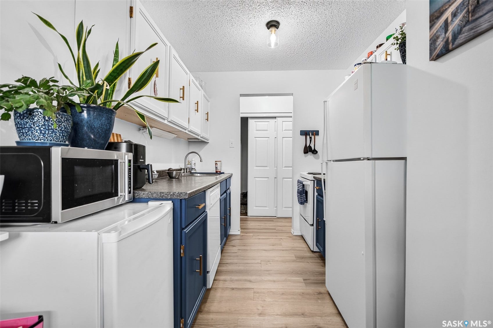 Galley kitchen featuring wood-finish flooring, white upper cabinetry, and blue lower cabinetry with gold-tone hardware