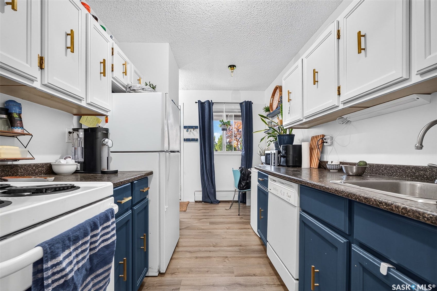 Kitchen featuring dual-toned cabinetry with gold-toned hardware, laminate countertops, wood-finish flooring, and a window with curtain