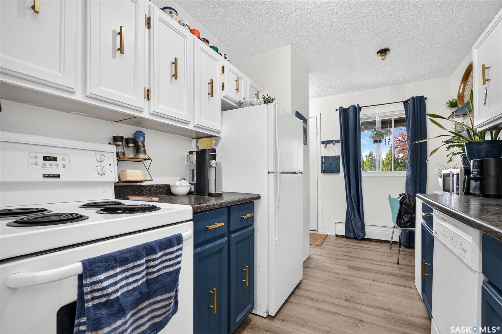 Kitchen featuring white upper cabinetry, blue lower cabinetry, gold-tone hardware, and wood-finish flooring