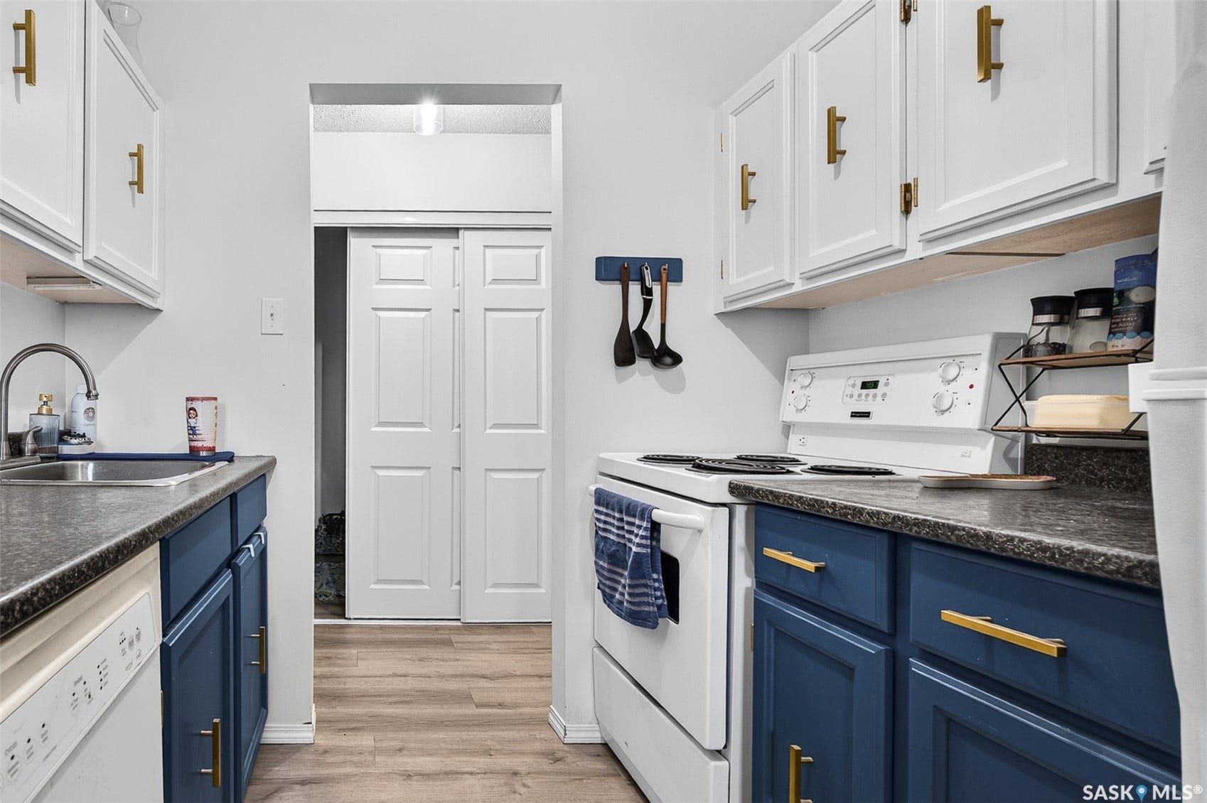 Galley kitchen featuring dual-tone cabinetry with gold-tone hardware, wood-finish flooring, a stainless steel sink, and a white electric range