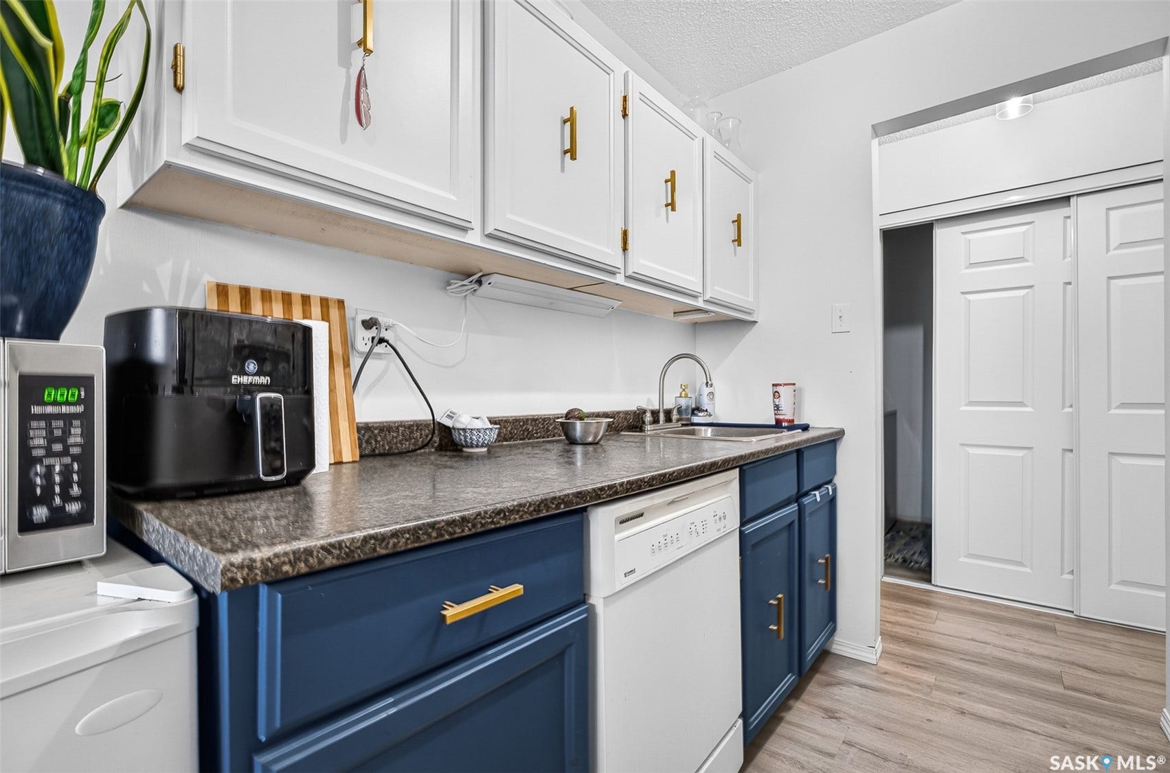 Kitchen featuring two-tone cabinetry with gold-tone hardware, a stainless steel sink, and light wood-finish flooring
