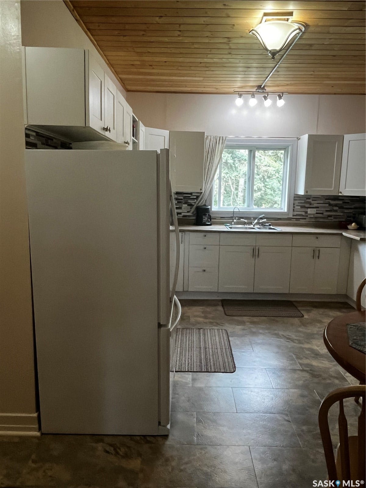 Wood-finish ceiling, white cabinetry, tile backsplash, stainless steel sink, and tile flooring