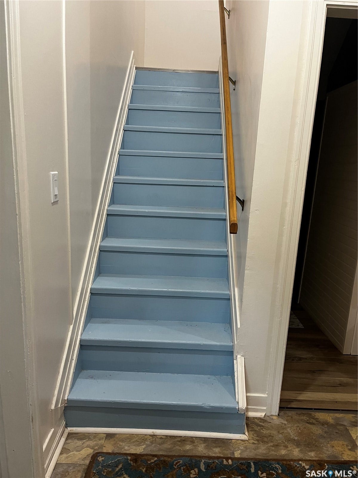 Staircase featuring blue-painted treads, a wood handrail, and white trim