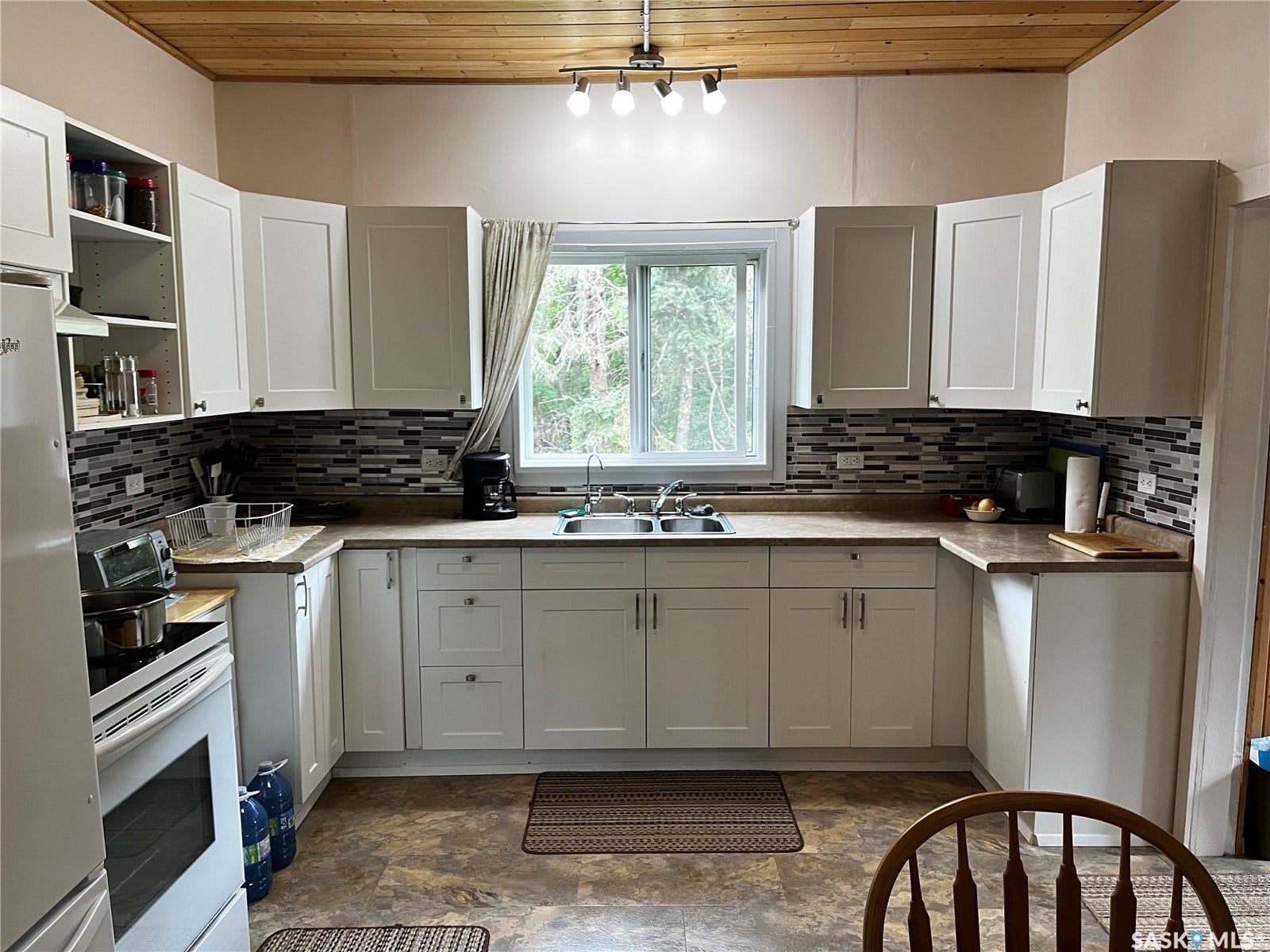 Bright, U-shaped kitchen featuring white cabinetry with ample storage, stainless steel appliances, dark tile backsplash, wood-finish countertops, and a large center window flooding the space with natural light