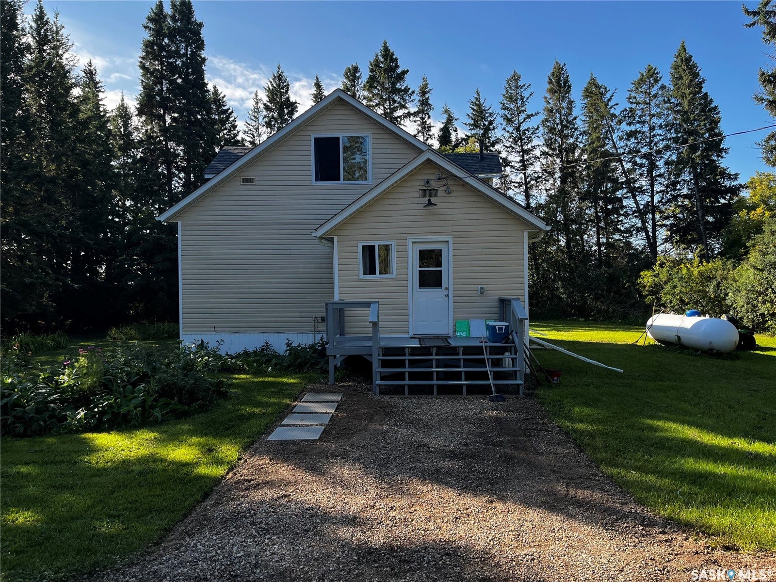 Two-story residence with light-colored siding, a gravel driveway, and a wooden deck leading to an exterior door