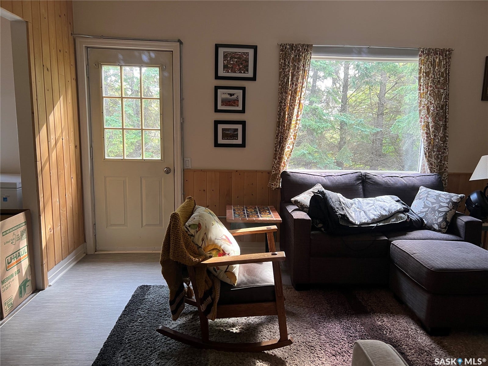 Light-toned wood paneling, white paneled door with glass inserts, large picture window, and wood-finish flooring