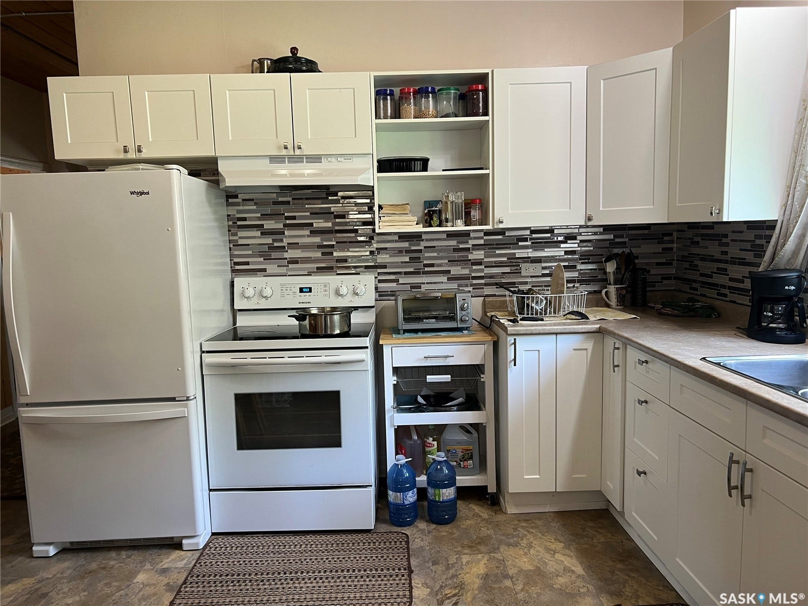 White shaker-style cabinetry, mosaic tile backsplash, wood-finish flooring, white appliances, and a stainless steel sink