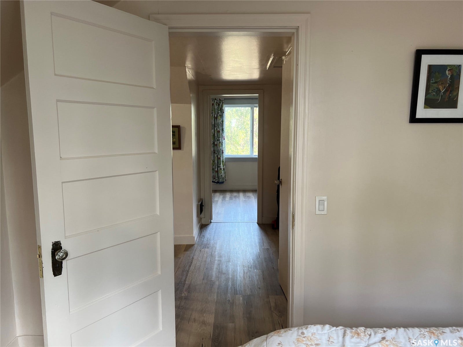 Wood-finish flooring throughout, white paneled doors with clear glass knobs, and a framed window offering natural light