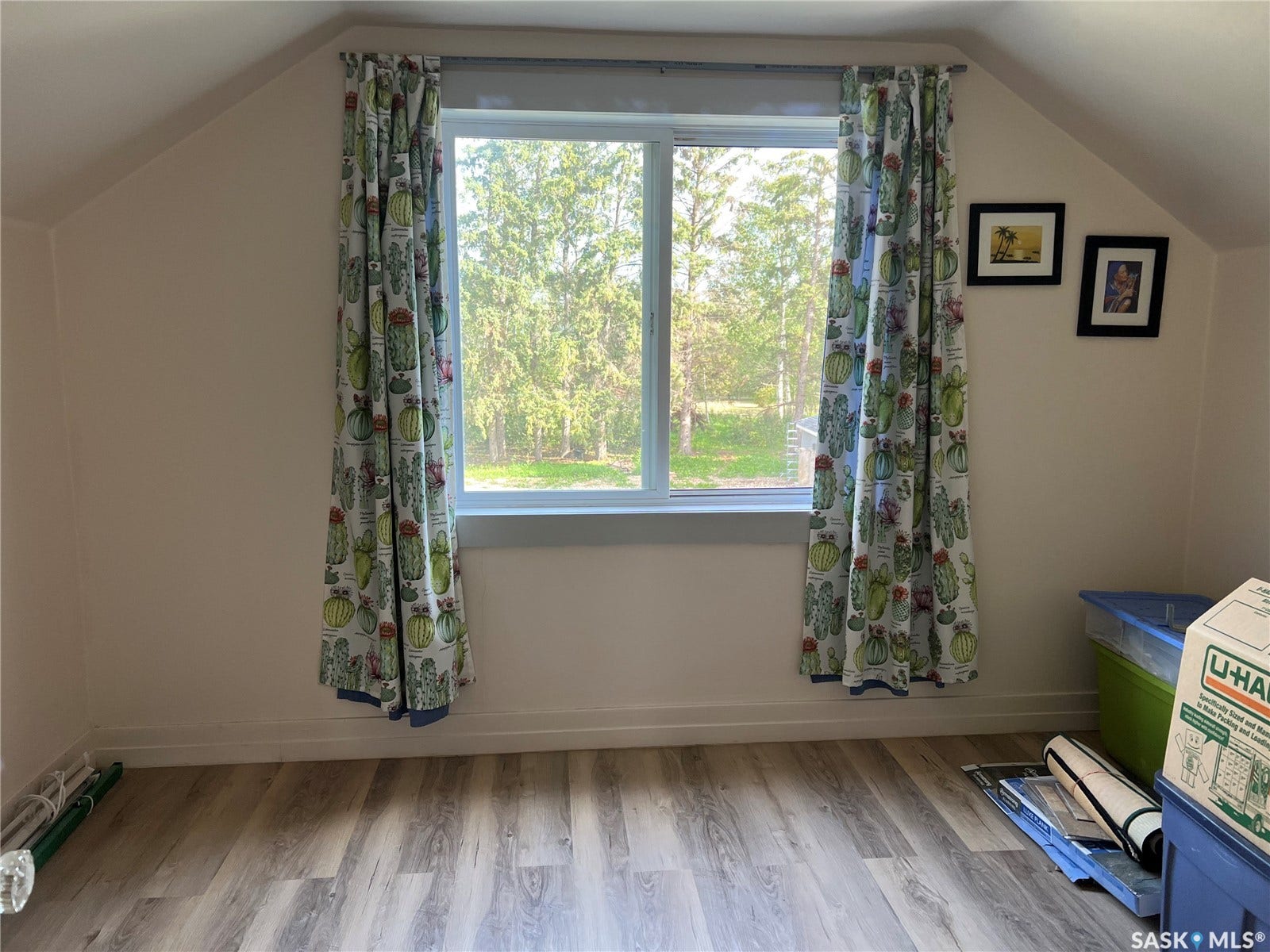 Sloped ceiling room featuring a window with natural light and wood-finish flooring