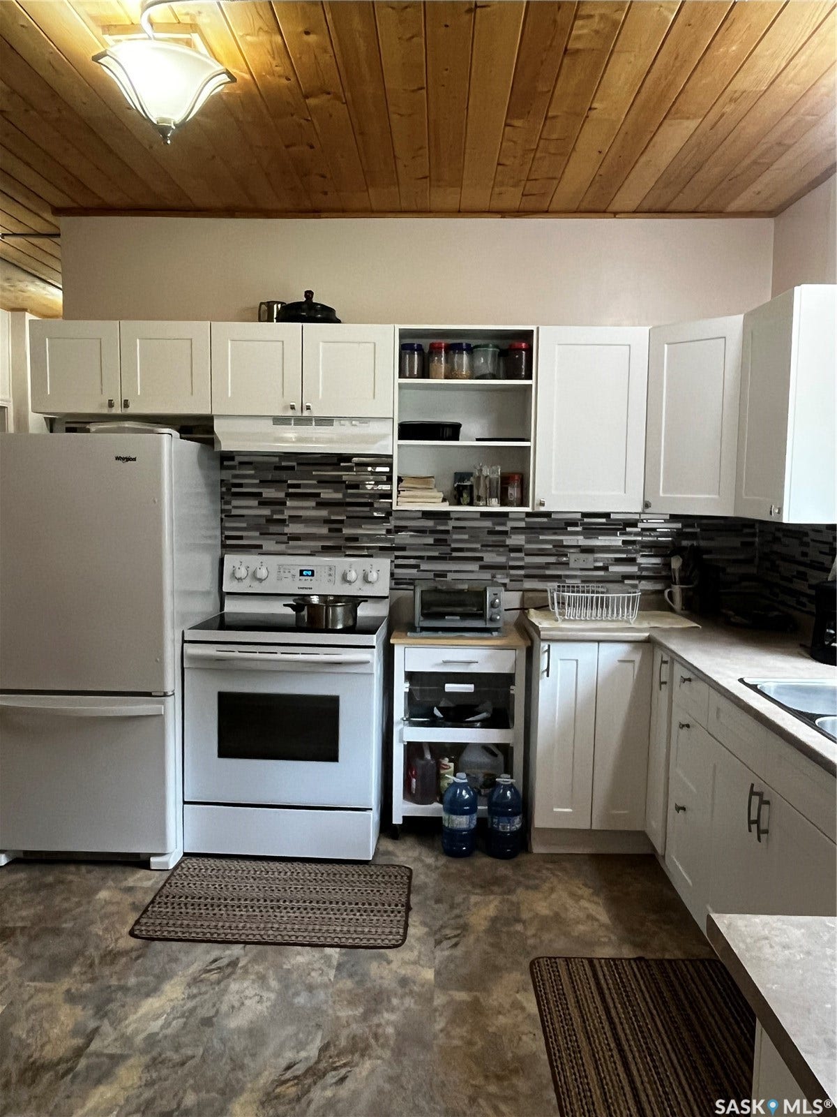Efficient galley kitchen featuring white cabinetry with ample storage, stainless steel refrigerator, electric range with backsplash, and wood-finish ceiling