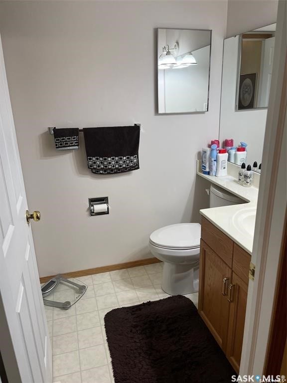 White flooring, wood-finish vanity with dual-door cabinetry, countertop with integrated sink, rectangular wall mirror with overhead lighting, and a white toilet