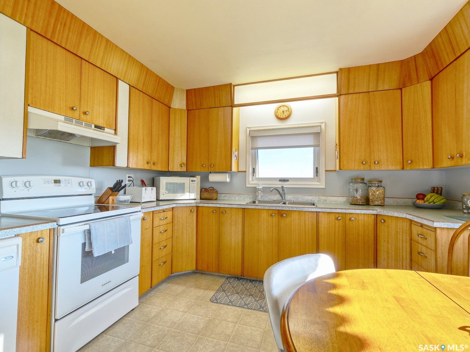 Wood-finish cabinetry with extensive storage, white appliances, and a window above the sink