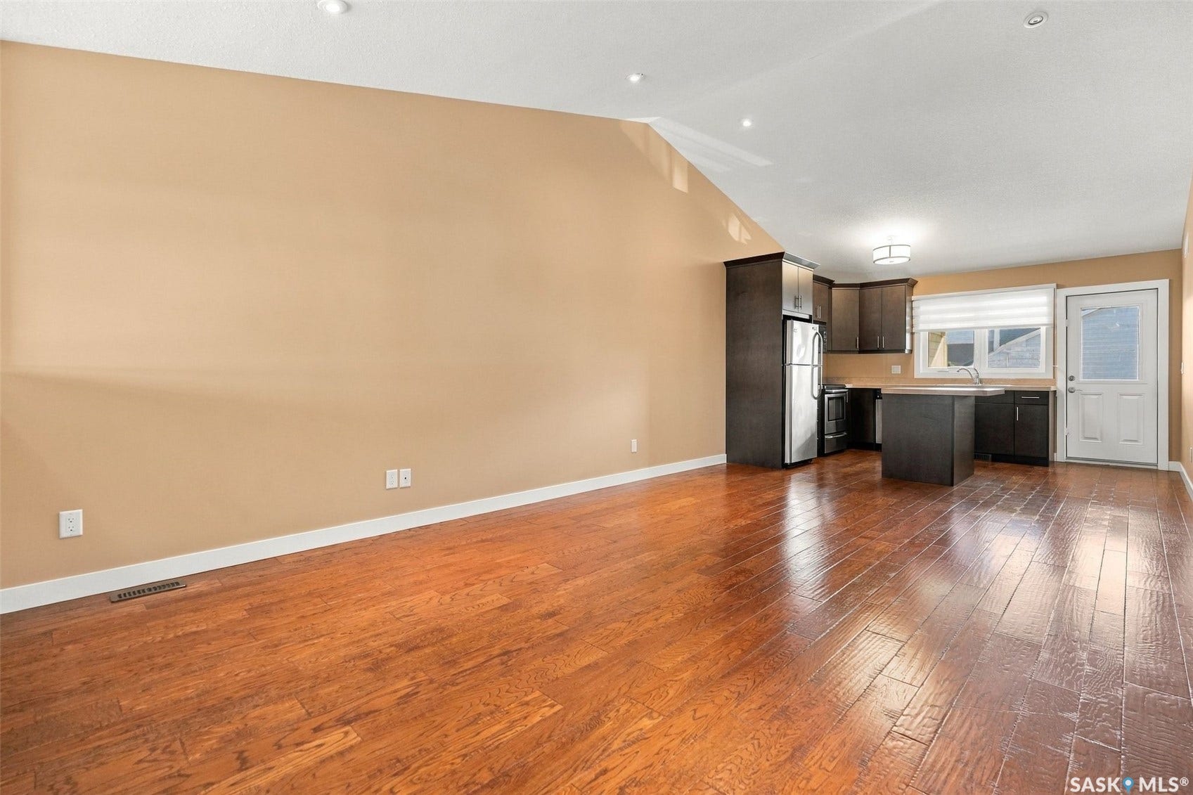 Wood-finish flooring throughout, vaulted ceiling, recessed lighting, dark wood-finish cabinetry, and stainless steel appliances
