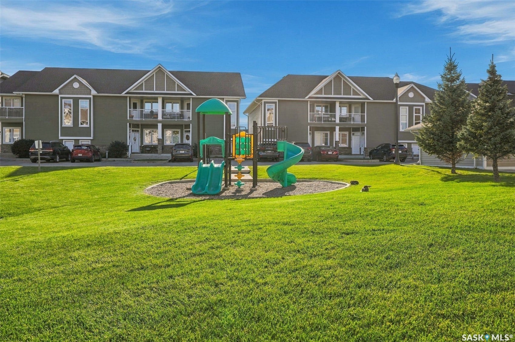 Expansive green space with a playground, framed by multi-level residential structures featuring balconies and gabled accents
