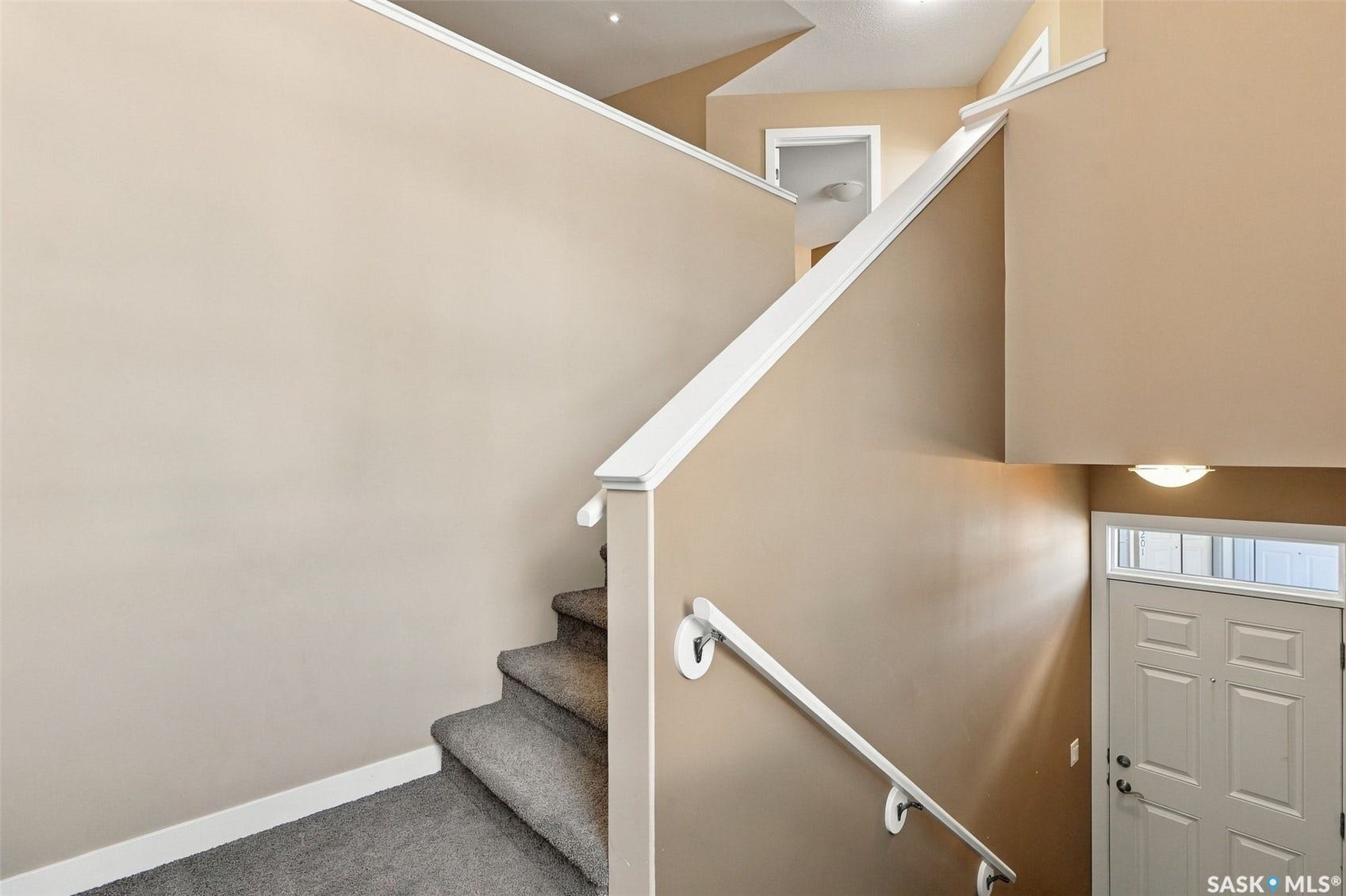 Carpeted staircase with white handrails and trim, leading to a paneled door with transom window