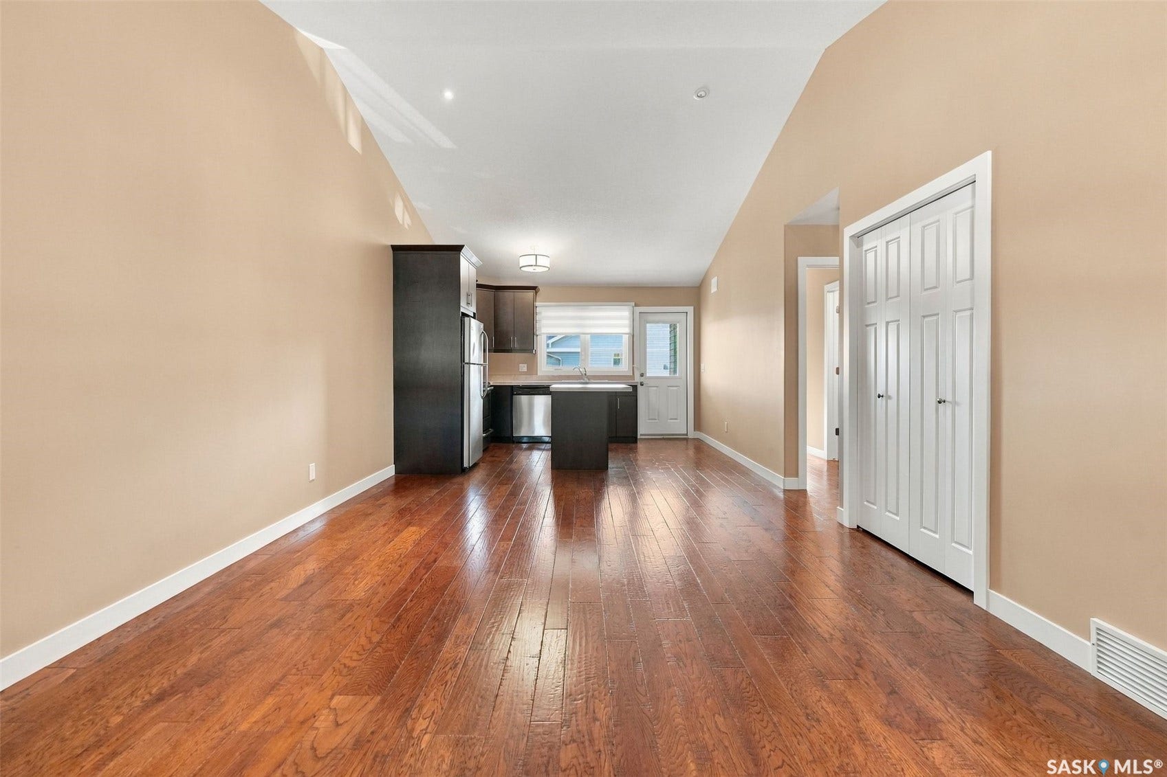 Hardwood-finish flooring, vaulted ceiling, kitchen island with stainless steel appliances, and a white paneled door