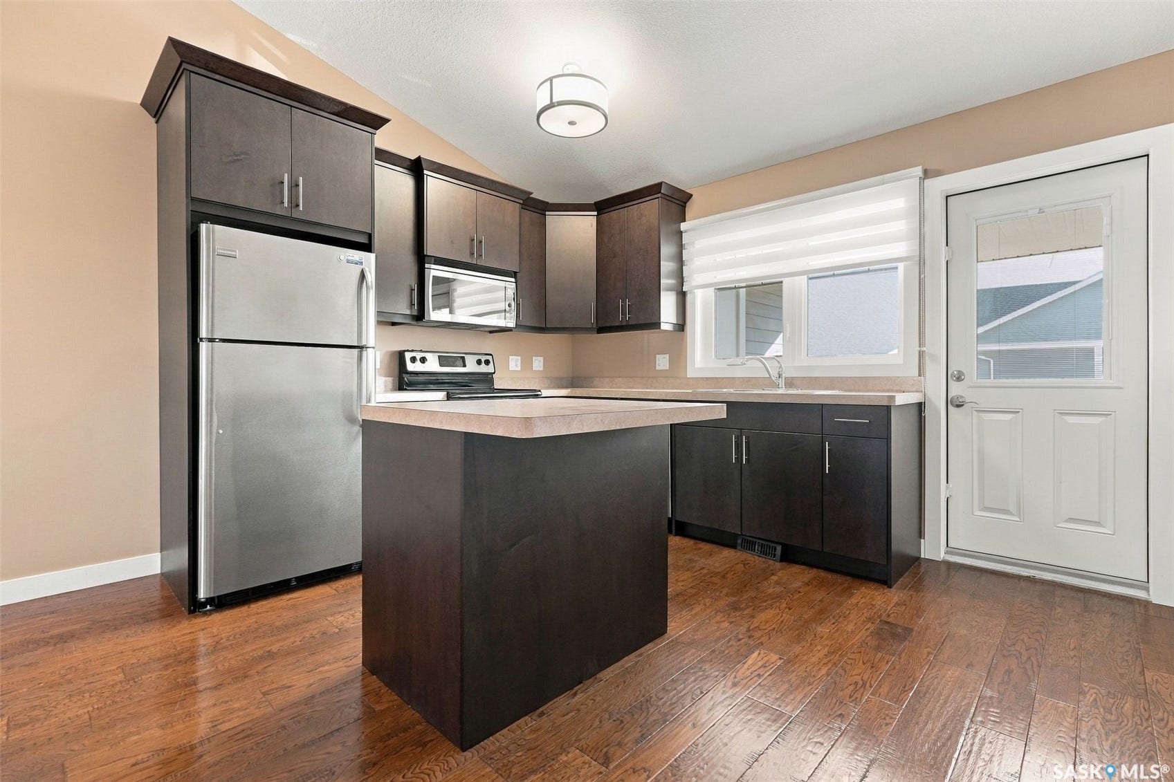 Kitchen featuring dark wood-finish cabinetry, stainless steel appliances, a center island with countertop, and wood-finish flooring