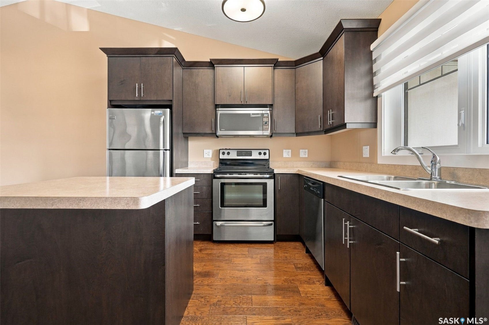 Kitchen featuring dark wood-finish cabinetry, light-toned countertops, stainless steel appliances, and wood-finish flooring