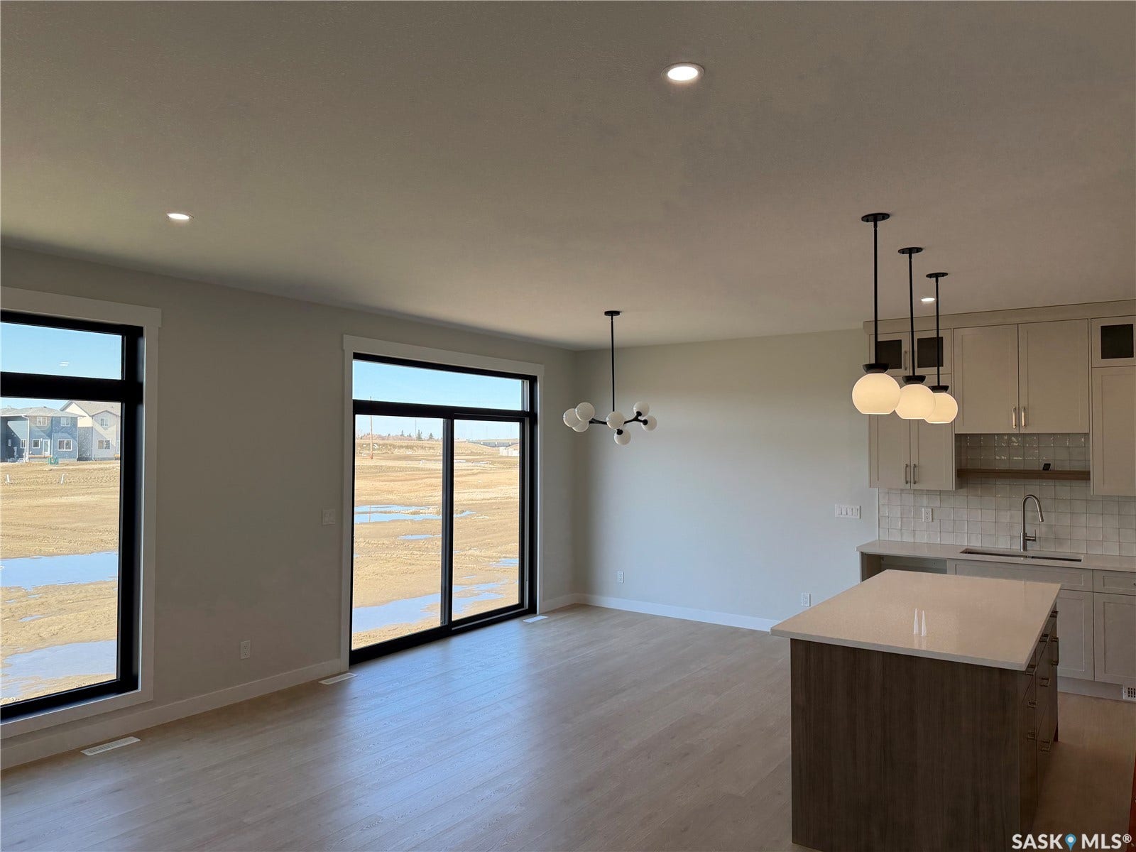 310 Traeger Manor, Saskatoon SK S7V 1Z4 Light wood-finish flooring, two large windows, sliding glass patio door, island with a light-colored countertop, and recessed lighting