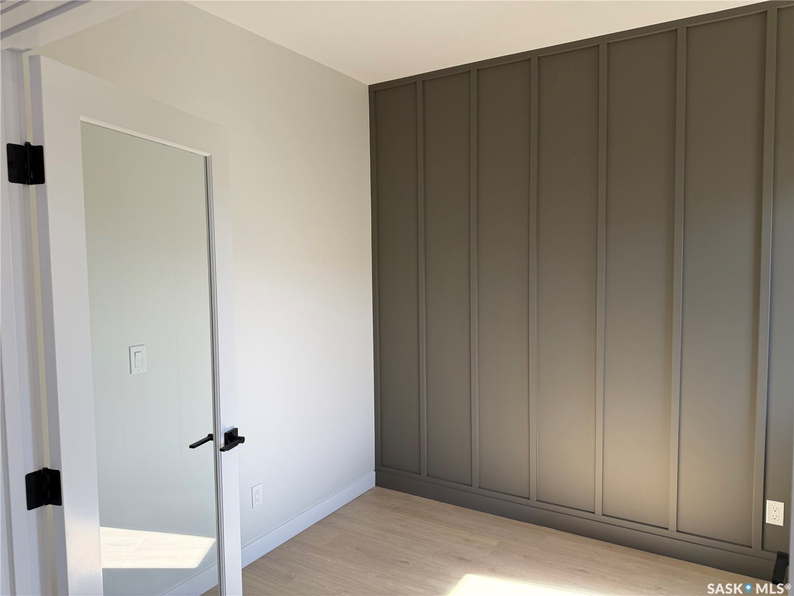 310 Traeger Manor, Saskatoon SK S7V 1Z4 Accent wall with vertical paneling, light wood-finish flooring, white walls, and a white door with matte black hardware