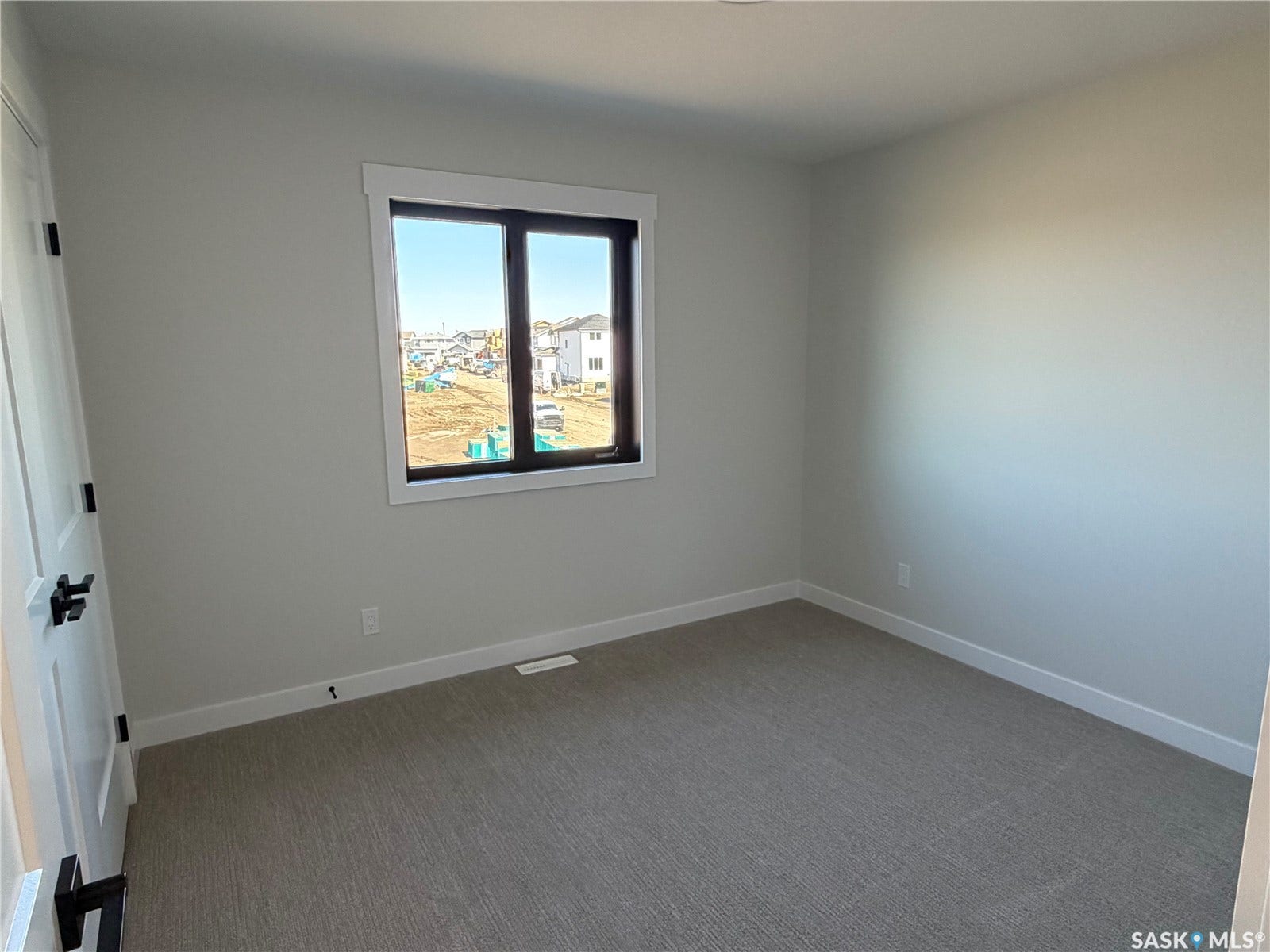 310 Traeger Manor, Saskatoon SK S7V 1Z4 Neutral tone walls, grey textured carpeting, white trim, and a window with a dark frame