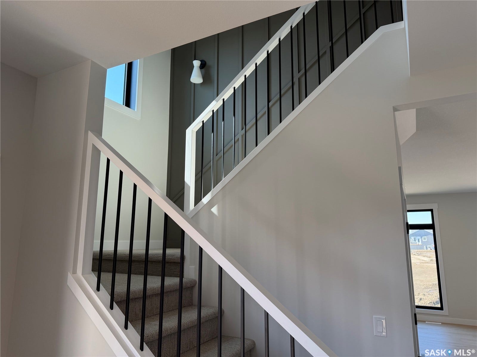 310 Traeger Manor, Saskatoon SK S7V 1Z4 Carpeted staircase with white handrails and black balusters, featuring a feature wall with vertical paneling and an attached wall sconce