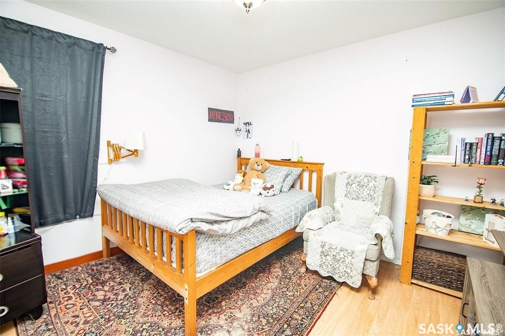 Bright secondary bedroom featuring warm wood-frame bed, wood-finish flooring, and ample natural light