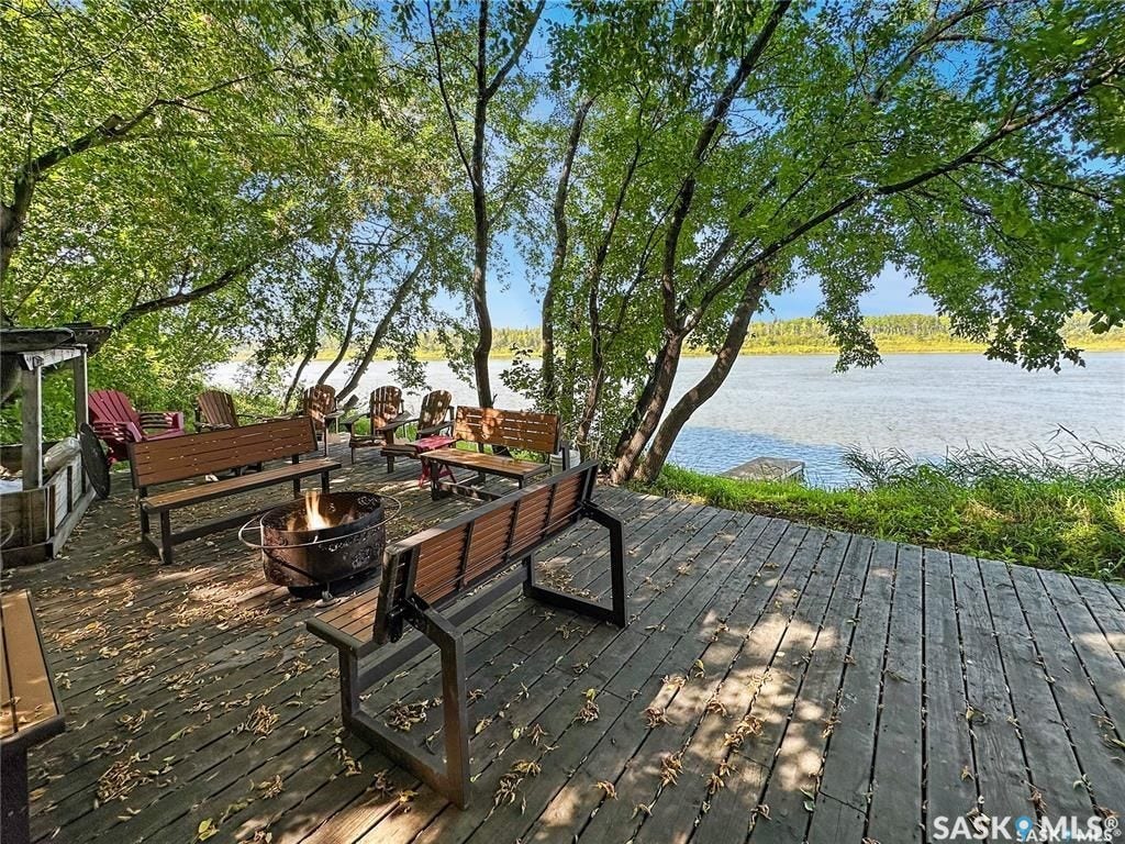 Expansive outdoor deck with a fire pit, surrounded by mature trees, and featuring waterfront access
