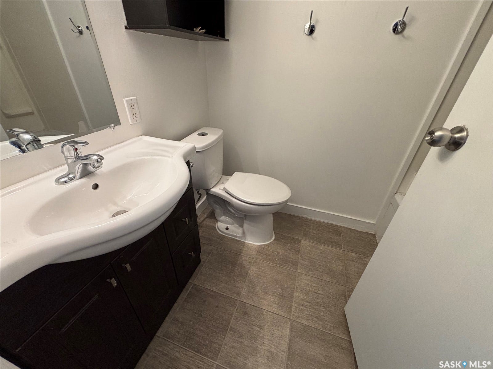 Pedestal sink with chrome faucet, dark wood-finish vanity, wall-mounted mirror, and neutral-toned floor tiling