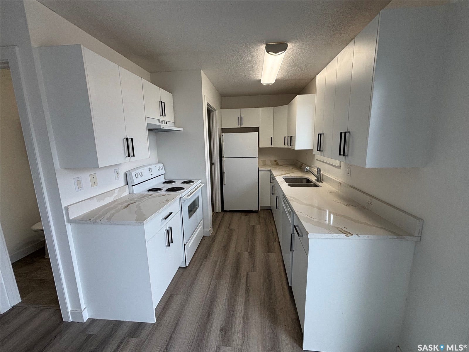 Galley kitchen featuring white cabinetry, light-toned countertops with veining, white appliances, and wood-finish flooring