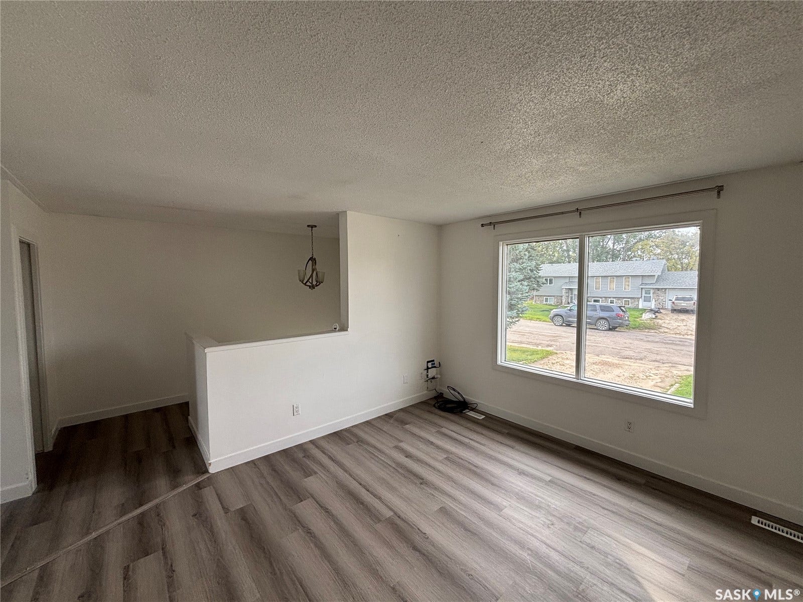 Wood-finish flooring, white painted walls, large window, and a decorative pendant light fixture