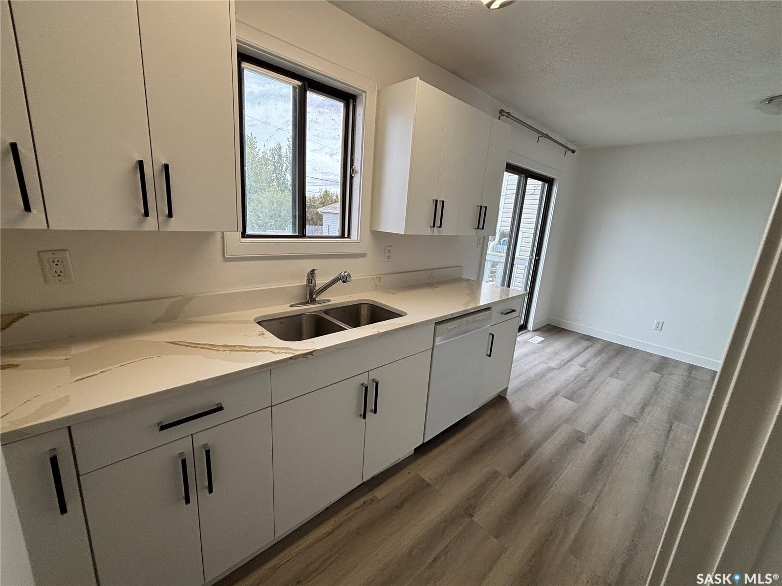 White cabinetry with black hardware, double basin stainless steel sink, patterned countertop, wood-finish flooring, and a sliding glass door